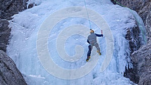 Athletic man with crampons and ice axes scales up the gorgeous frozen waterfall.