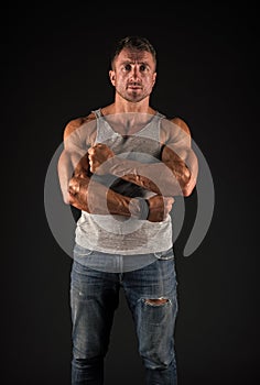 Athletic man cross strong muscular arms with biceps triceps muscles in casual wear black background, sportsman