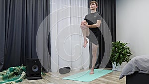 Athletic man does gymnastics exercises on mat. Young energetic male exercising on yoga mat. Fitness trainer doing stretch training