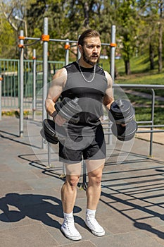 Athletic man doing arms weight lifting dumbbells exercises, pumping up arm bicep muscles outdoors