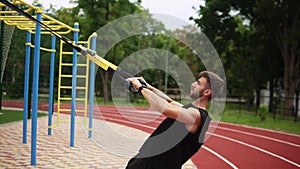 An athletic man doing biceps exercise using rubber belt to force strenth of workout outdoors