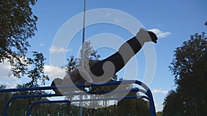 Athletic man doing gymnastics elements on bar in city park. Male sportsman performs strength exercises during workout