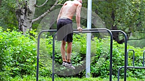 Athletic man doing gymnastics elements on bars in City Park