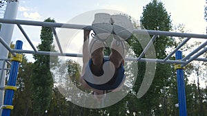 Athletic man doing gymnastics elements on horizontal bar in city park. Male sportsman performs strength exercises during