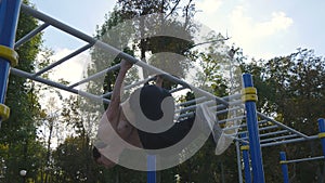 Athletic man doing gymnastics elements on horizontal bar in city park. Male sportsman performs strength exercises during
