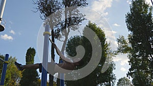 Athletic man doing gymnastics elements on horizontal bar in city park. Male sportsman performs strength exercises during