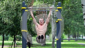 Athletic man doing lifting legs on horizontal bar in City Park. Athletic man exercise the abdominals on horizontal bar