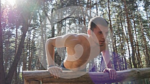 Athletic man doing push ups from log at the forest. Strong young muscular guy training outdoor at the wood in summer