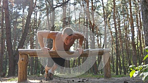 Athletic man doing push ups from log at the forest. Strong young muscular guy training outdoor at the wood in summer