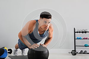 Athletic man doing push ups with medicine ball in modern gym, space for text