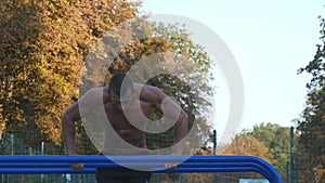 Athletic man doing push ups on parallel bars at sports ground in city park. Strong young muscular guy training outdoor