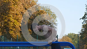 Athletic man doing push ups on parallel bars at sports ground in city park. Strong young muscular guy training outdoor