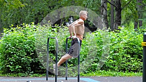 Athletic man doing pushups on bars in City Park. side view. Workout.