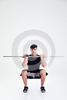 Athletic man doing squatting exercises with barbell