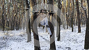 Athletic man doing static exercises on horizontal bar at forest. Sportive guy training abdominal outdoor. Young