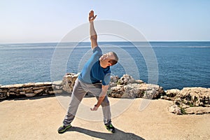 Athletic man doing stretching exercise, preparing for workout on seashore. Handsome fitness athlete doing a stretching routine.