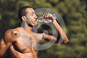 Athletic man drinking water after workout outdoors
