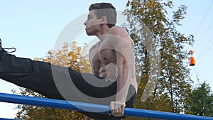 Athletic man exercise the abdominals on bar in city park. Male sportsman performs strength exercises during workout