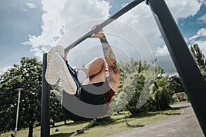 Athletic man hanging upside down on outdoor pull-up bar in a sunny urban park