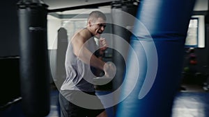 Athletic man has workout and punching boxing bag in gym