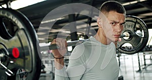 Athletic man hold heavy barbell on shoulders and looking at camera at gym