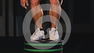 Athletic man jumping in gym. Crossfit training workout. Male with naked torso exercises jump on the dark background.