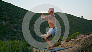 Athletic man practicing spiritual yoga in evening mountains. Fit guy meditating