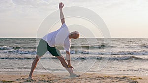 Athletic man practicing yoga in extended triangle asana on sea shore