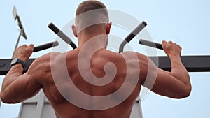 Athletic Man Pumps Up Muscles Doing Pull-Ups Open Sports Ground with Bare Torso