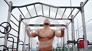 Athletic Man Pumps Up Muscles Doing Pull-Ups Open Sports Ground with Bare Torso
