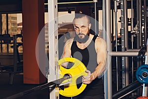 Athletic man puts on plate for barbell in the gym