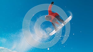 Athletic man in red winter jacket snowboarding and doing tricks in the air.