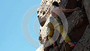 Athletic man rock climber climbs on a cliff, reaching and gripping hold.