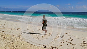 Athletic man run along ocean surf by sandy beach