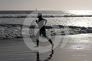 athletic man runner silhouette run on summer beach with sea water and sun, motivation