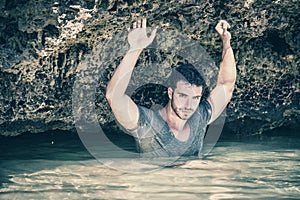 Athletic man in the sea or ocean by rocks, wet t-shirt