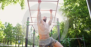 Athletic man shirtless swinging exercising on monkey bar at sports ground in park. Fitness sport traning on brachiation