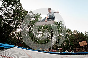 Athletic man with skateboard simulator jumps on trampoline against the backdrop of green trees