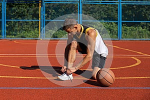 Athletic man standing on basketball court ties his shoelaces before playing game.
