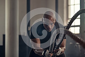 Athletic man using battle rope at gym