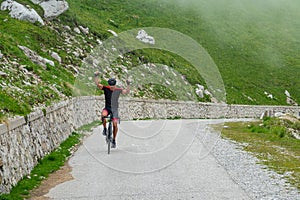 Athletic man victoriously lifts his arms while cycling up a mountain road.