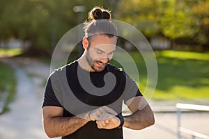 Athletic man wearing activewear monitors his workout with smartwatch outdoors