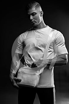 Athletic man in white t-shirt with bag over his shoulder in studio