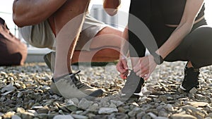 Athletic man in white t-shirt and woman in black top tying shoelaces.