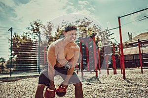 Athletic man working out with a kettlebell at street gym yard. Strength and motivation.