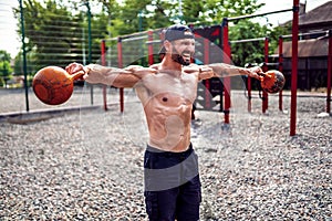 Athletic man working out with a kettlebell at street gym yard. Strength and motivation.