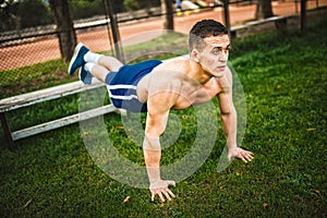 Athletic man during workout in park. Fitness personal trainer doing pushups on grass. Cross-fit training concept