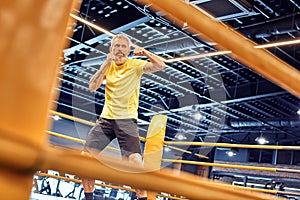 Athletic mature man in sportswear boxing while standing on the ring at gym