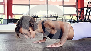 Athletic mature woman is doing set of reps push-ups from the floor in gym.