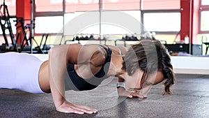 Athletic mature woman is doing set of reps push-ups from the floor in gym.